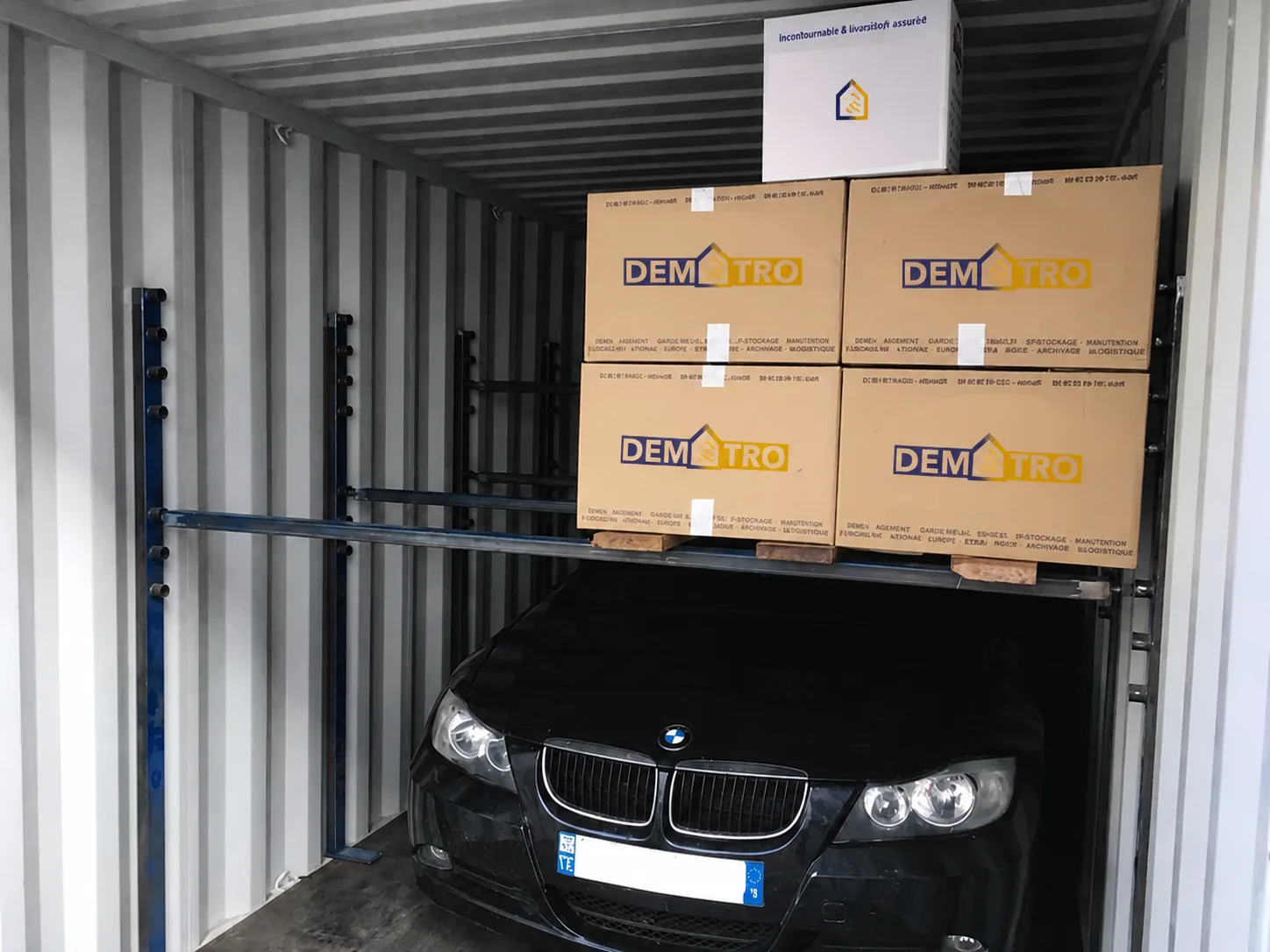 Voiture particulière arrimée dans un conteneur maritime aux côtés de cartons de déménagement Demetro, prête pour l'export vers les DOM-TOM
